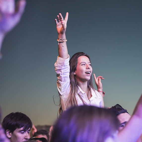 Une jeune festivalière lève la main vers le ciel dans la foule